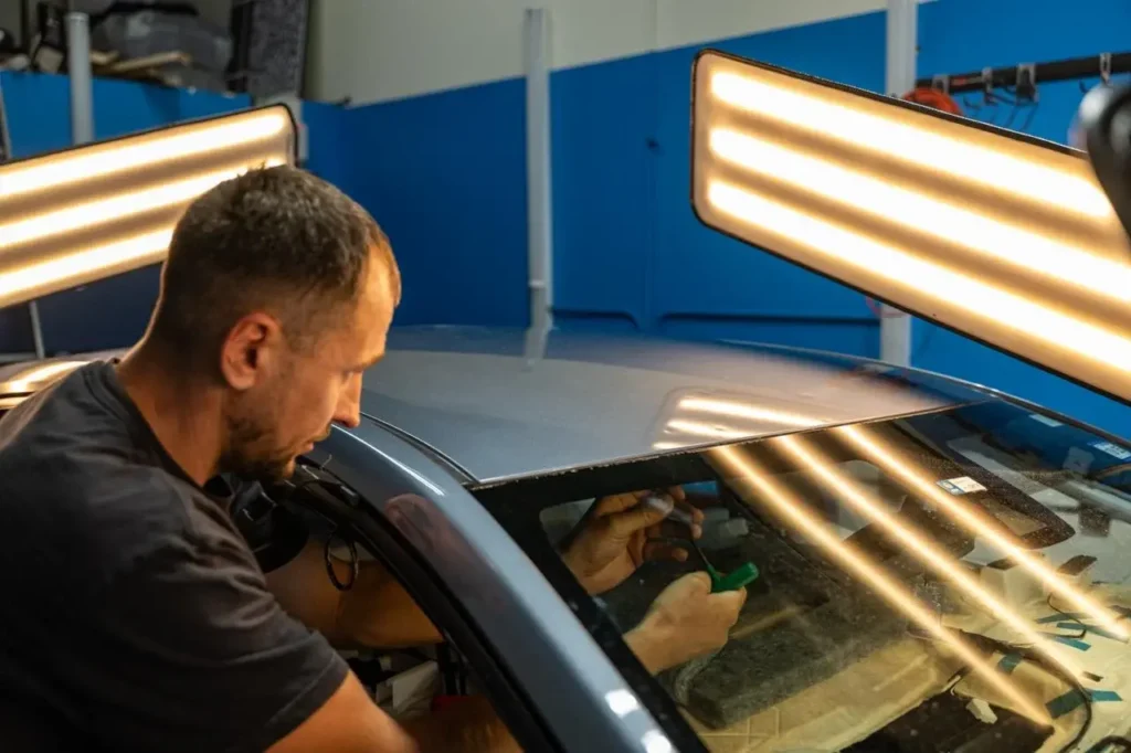 EZ Tech technician repairing car roof dent with PDR tools and lighting.