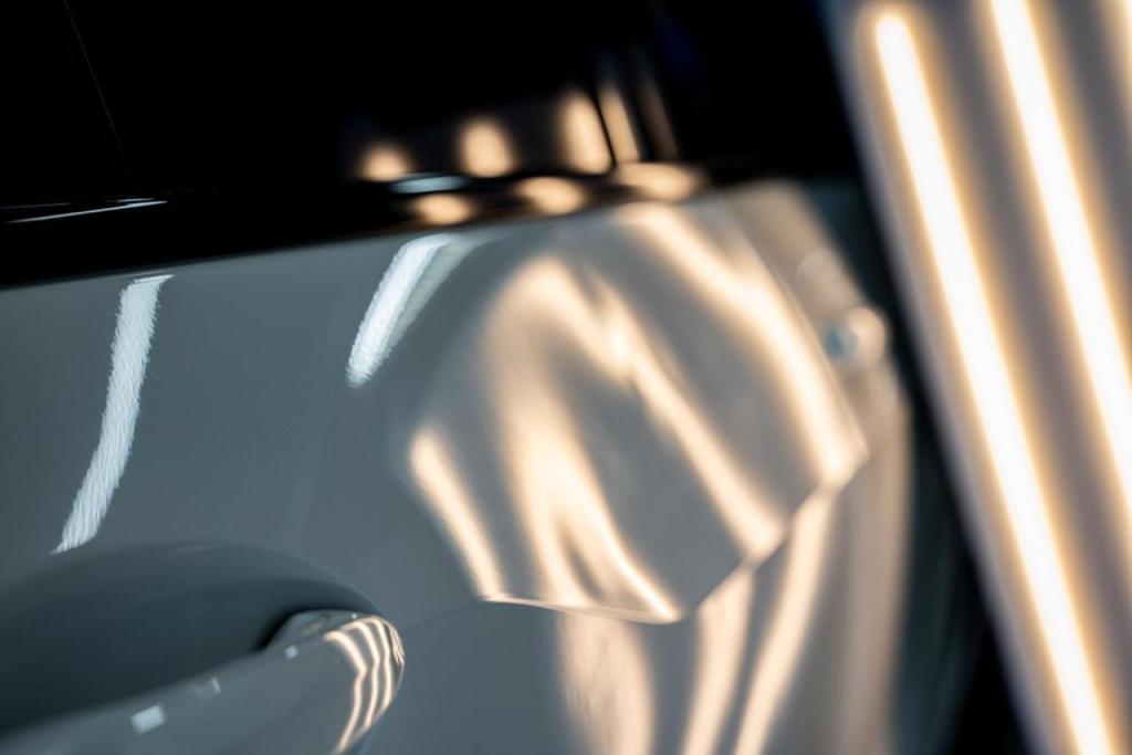 Paintless dent repair tools and lighting highlighting body line dent on a white car door.