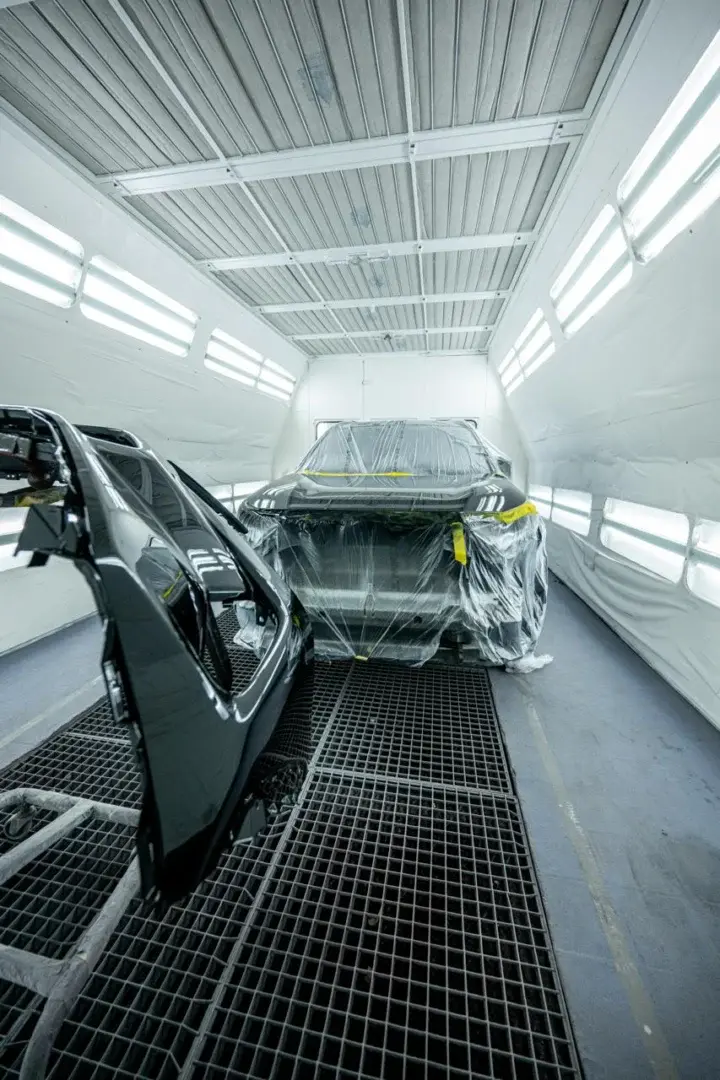 Vehicle in paint booth undergoing body panel restoration and painting.