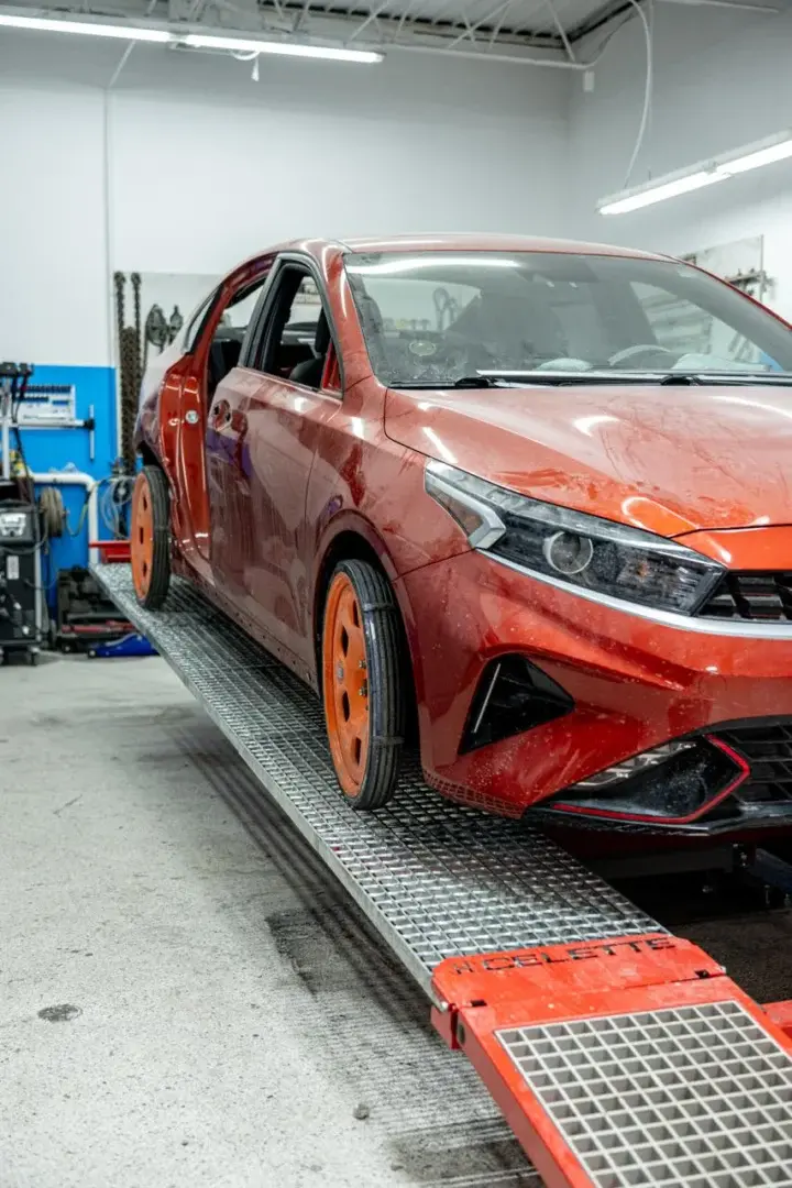 Red Kia car on lift in auto repair shop for paintless dent repair.