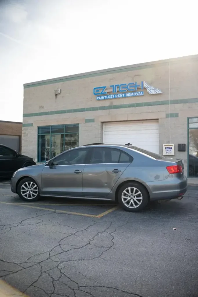 EZ Tech Paintless Dent Removal facility and gray sedan undergoing body panel replacement.