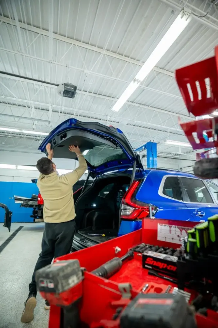 EZ Tech technician working at the open liftgate of a blue SUV in the shop, next to a red tool cart