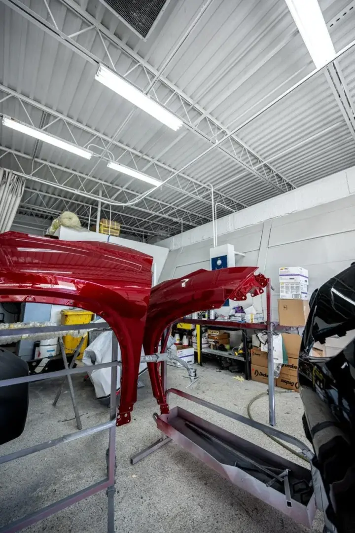 Two red painted fenders on stands in a body shop bay, next to the side of a black vehicle